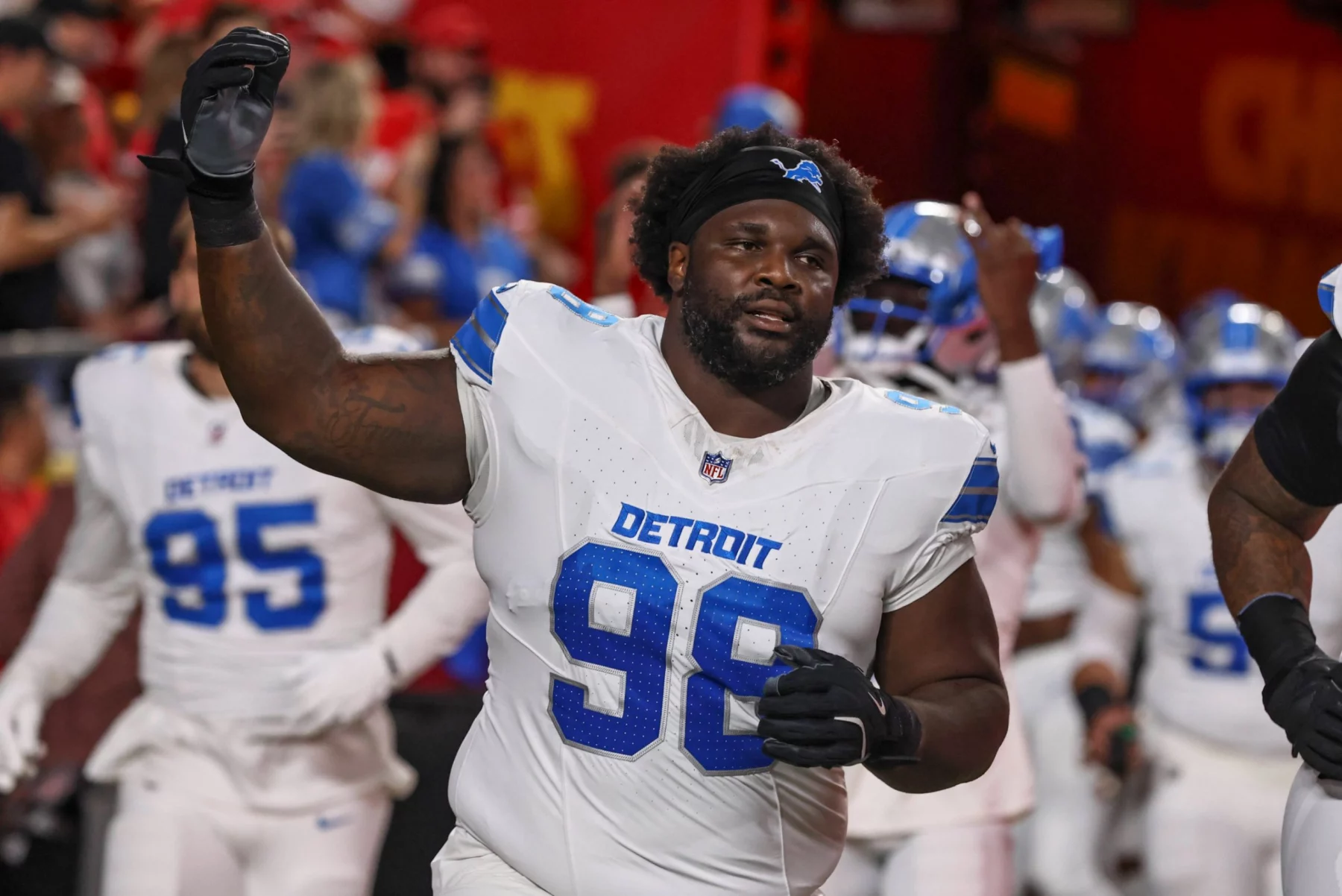 DJ Reader - Ein Innenverteidiger der Detroit Lions in einem weißen Trikot mit der Nummer 98 hebt seinen Arm auf dem Spielfeld, während im Hintergrund Teamkollegen und eine Menschenmenge zu sehen sind. Er wird vor der Free Agency 2026 für Aufsehen sorgen. Alt-Text wurde KI-generiert.