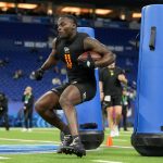 Jeremiyah Love - Ein Football-Spieler in Sportkleidung läuft mit einem Ball und manövriert um blaue Tackling-Attrappen während einer Übung auf einem Hallenfeld, ähnlich wie die QBs und WRs beim NFL Scouting Combine. Alt-Text wurde KI-generiert.