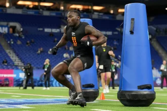 Jeremiyah Love - Ein Football-Spieler in Sportkleidung läuft mit einem Ball und manövriert um blaue Tackling-Attrappen während einer Übung auf einem Hallenfeld, ähnlich wie die QBs und WRs beim NFL Scouting Combine. Alt-Text wurde KI-generiert.