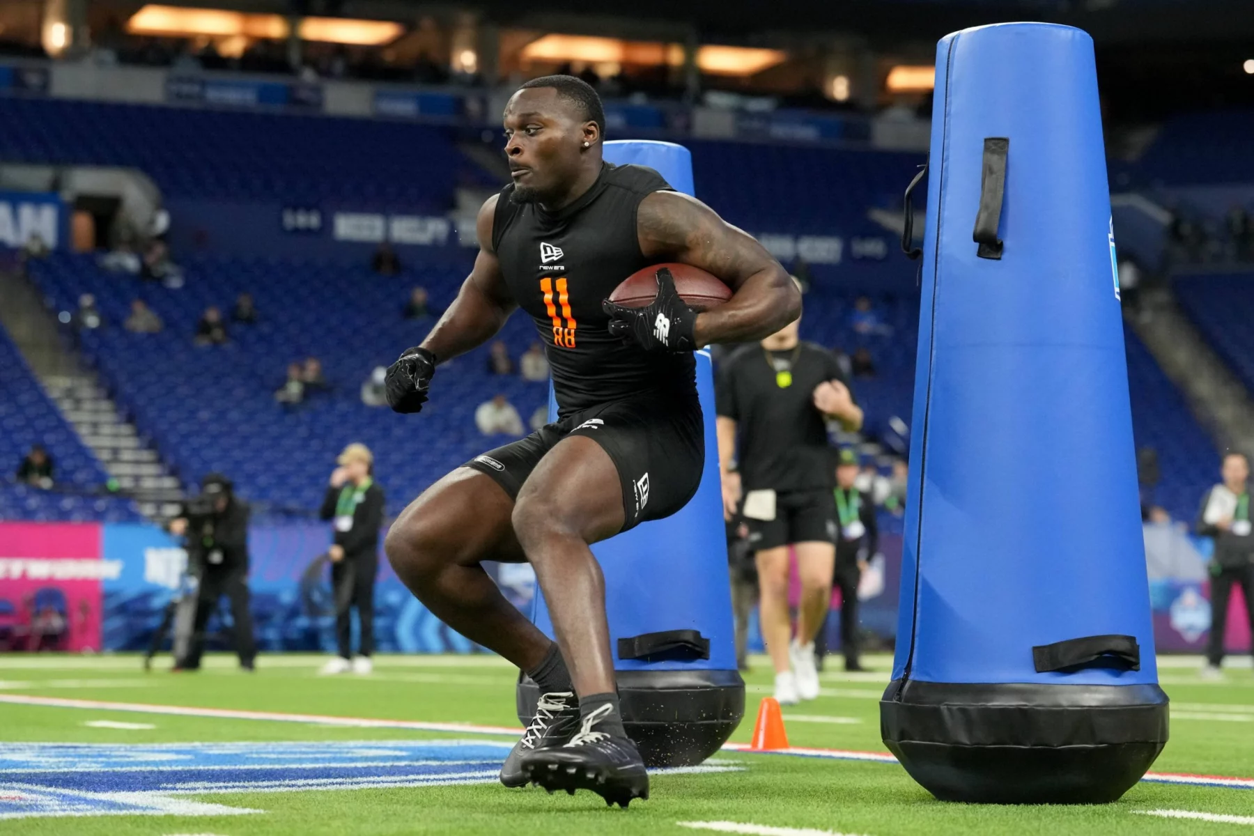 Jeremiyah Love - Ein Football-Spieler in Sportkleidung läuft mit einem Ball und manövriert um blaue Tackling-Attrappen während einer Übung auf einem Hallenfeld, ähnlich wie die QBs und WRs beim NFL Scouting Combine. Alt-Text wurde KI-generiert.