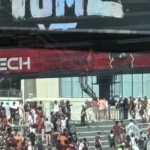Vor einem Gebäude in der Nähe des Lane Stadium versammelt sich eine Menschenmenge, viele in kastanienbrauner Kleidung, unter einem "VIRGINIA TECH"-Banner und einem teilweise sichtbaren "HOME"-Schild darüber. Alt-Text wurde KI-generiert.