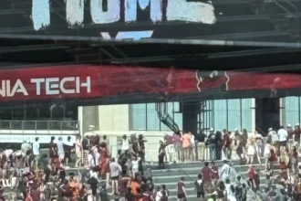 Vor einem Gebäude in der Nähe des Lane Stadium versammelt sich eine Menschenmenge, viele in kastanienbrauner Kleidung, unter einem "VIRGINIA TECH"-Banner und einem teilweise sichtbaren "HOME"-Schild darüber. Alt-Text wurde KI-generiert.