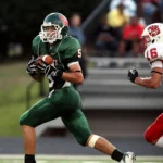 Ein Football-Spieler in einem grünen Trikot rennt mit dem Ball, während ein Spieler in einem rot-weißen Trikot aus Österreich ihn auf dem Spielfeld verfolgt und so den Geist des American Football und den wachsenden NFL-Hype einfängt. Alt-Text wurde KI-generiert.