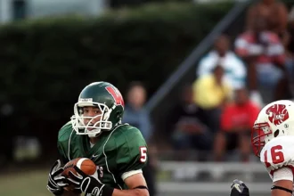 Ein Football-Spieler in einem grünen Trikot rennt mit dem Ball, während ein Spieler in einem rot-weißen Trikot aus Österreich ihn auf dem Spielfeld verfolgt und so den Geist des American Football und den wachsenden NFL-Hype einfängt. Alt-Text wurde KI-generiert.