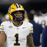 Ein Football-Spieler in einem weiß-gelben Cal-Trikot mit der Nummer 1 und einem Helm steht auf dem Spielfeld - Jaydn Ott zeigt sein Können und zieht damit im Vorfeld des NFL Draft 2026 die Aufmerksamkeit auf sich. Alt-Text wurde KI-generiert.