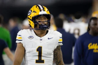 Ein Football-Spieler in einem weiß-gelben Cal-Trikot mit der Nummer 1 und einem Helm steht auf dem Spielfeld - Jaydn Ott zeigt sein Können und zieht damit im Vorfeld des NFL Draft 2026 die Aufmerksamkeit auf sich. Alt-Text wurde KI-generiert.