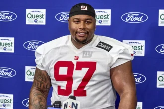 Der Spieler der New York Giants, Dexter Lawrence (Nummer 97), steht während einer Presseveranstaltung an einem Podium mit Mikrofonen und diskutiert möglicherweise über die Spielzüge des Teams im Vorfeld des NFL Draft 2026. Alt-Text wurde KI-generiert.
