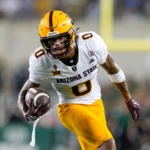 Jordyn Tyson - Ein Wide Receiver der Arizona State University in einer weiß-gelben Uniform läuft während eines Spiels mit Helm und Handschuhen mit dem Ball und zeigt seine Fähigkeiten vor dem NFL Draft 2026. Alt-Text wurde KI-generiert.