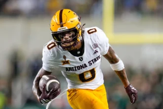 Jordyn Tyson - Ein Wide Receiver der Arizona State University in einer weiß-gelben Uniform läuft während eines Spiels mit Helm und Handschuhen mit dem Ball und zeigt seine Fähigkeiten vor dem NFL Draft 2026. Alt-Text wurde KI-generiert.