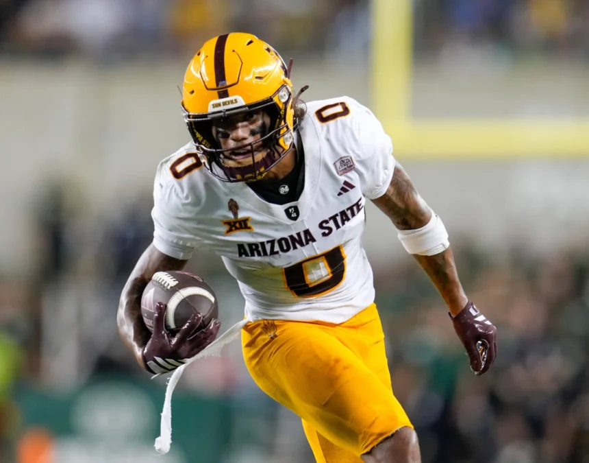Jordyn Tyson - Ein Wide Receiver der Arizona State University in einer weiß-gelben Uniform läuft während eines Spiels mit Helm und Handschuhen mit dem Ball und zeigt seine Fähigkeiten vor dem NFL Draft 2026. Alt-Text wurde KI-generiert.