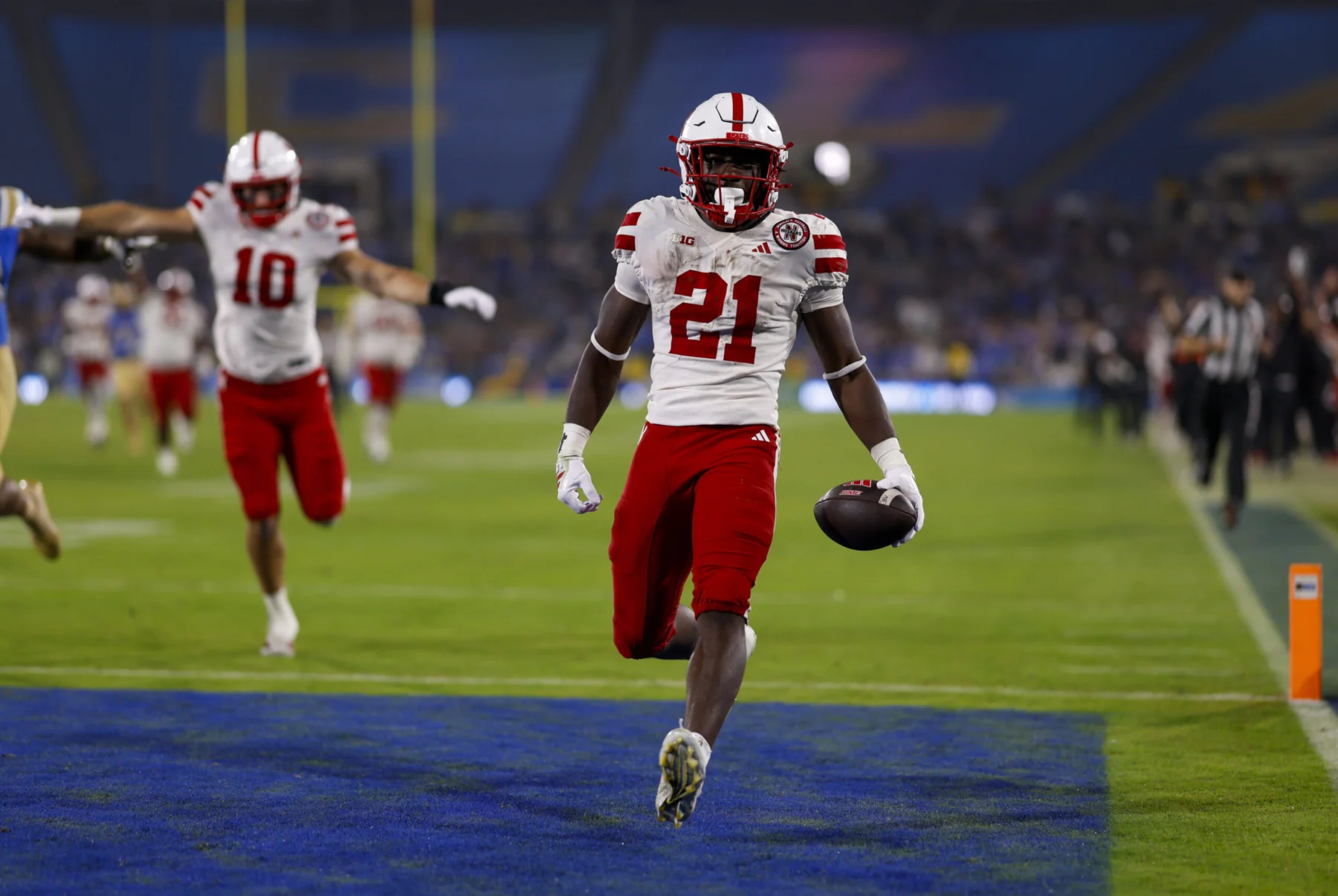 Ein Football-Spieler in einem rot-weißen Trikot rennt mit dem Ball in die Endzone, während seine Teamkollegen im Hintergrund feiern - ein elektrisierender Moment, der Emmett Johnsons Spielerprofil vor dem NFL Draft 2026 prägen könnte. Alt-Text wurde KI-generiert.