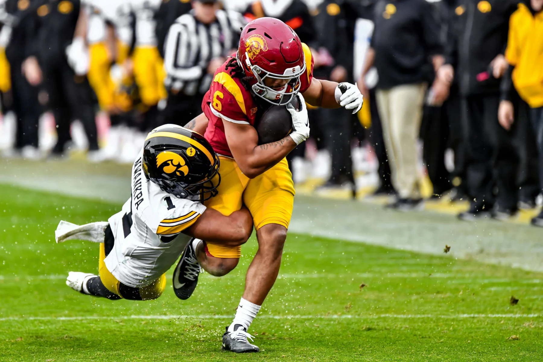 Makai Lemon - Ein Wide Receiver in Gelb und Rot versucht, während eines Spiels einen Tackle eines Spielers in Weiß und Schwarz zu durchbrechen, während im Hintergrund Schiedsrichter und andere Spieler zu sehen sind - ein actiongeladener Moment vor dem NFL Draft 2026. Alt-Text wurde KI-generiert.