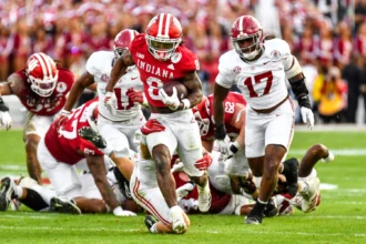 RB Kaelon Black, ein herausragender College-Football-Spieler aus Indiana, läuft mit dem Ball, während Verteidiger von Alabama ihn während eines Spiels verfolgen. Im Hintergrund sind Spieler und Schiedsrichter zu sehen, die sein Potenzial für den NFL-Draft 2026 unterstreichen. Alt-Text wurde KI-generiert.