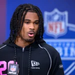 Ein Footballspieler, der einen schwarzen Kapuzenpulli trägt, spricht während des NFL Scouting Combine an einem NFL-Mikrofon und hofft, die Scouts vor dem NFL Draft 2026 zu beeindrucken und in die Riege der besten Cornerbacks aufgenommen zu werden. Alt-Text wurde KI-generiert.
