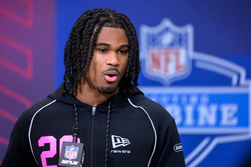 Ein Footballspieler, der einen schwarzen Kapuzenpulli trägt, spricht während des NFL Scouting Combine an einem NFL-Mikrofon und hofft, die Scouts vor dem NFL Draft 2026 zu beeindrucken und in die Riege der besten Cornerbacks aufgenommen zu werden. Alt-Text wurde KI-generiert.