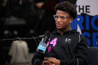 Caleb Downs - Ein Mann mit Brille und schwarzem Kapuzenpulli mit der Nummer 34 sitzt in einer Studioumgebung und spricht in ein Mikrofon mit der Aufschrift "Disney+", um über Safeties und ihre Aussichten für den NFL Draft 2026 zu sprechen. Alt-Text wurde KI-generiert.