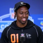 Ein Mann in einem schwarzen NFL-Kapuzenpulli und einer Mütze spricht an einem Mikrofon mit einem NFL Draft 2026 im Hintergrund, möglicherweise über Kaytron Allens Spielerprofil. Alt-Text wurde KI-generiert.