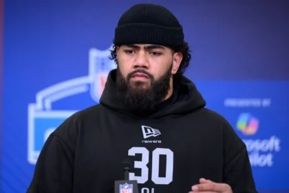 Ein Mann mit Bart und schwarzer Mütze, der einen schwarzen Kapuzenpulli mit der Nummer 30 trägt, steht bei einer Veranstaltung vor einer Kulisse für den NFL Draft 2026. Alt-Text wurde KI-generiert.