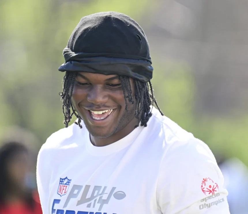 Eine Person, die eine schwarze Kopfbedeckung und ein weißes NFL-Trikot mit einem Special Olympics-Logo trägt, lächelt an einem sonnigen Tag im Freien und inspiriert künftige Edge Rusher im Vorfeld des NFL Draft 2026. Alt-Text wurde KI-generiert.