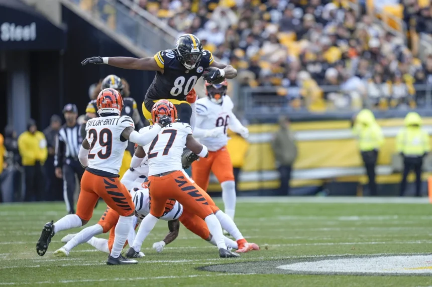 Ein Spieler der Pittsburgh Steelers, inspiriert von Darnell Washington kürzlicher Vertragsverlängerung, springt während eines Footballspiels an einem sonnigen Tag über zwei Verteidiger der Cincinnati Bengals. Alt-Text wurde KI-generiert.