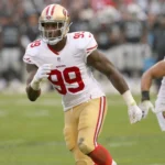 Aldon Smith, der das weiß-rote Trikot der San Francisco 49ers mit der Nummer 99 trägt, rennt während eines Spiels über das Spielfeld. Alt-Text wurde KI-generiert.