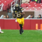 Der Footballspieler Ahmad Hardy aus Missouri läuft während eines Spiels gegen Arkansas mit dem Ball über den regennassen Rasen, während sich von links ein Verteidiger nähert – und beweist damit seine Widerstandsfähigkeit, obwohl er sich erst kürzlich von einer Schussverletzung erholt hat. Alt-Text wurde KI-generiert.