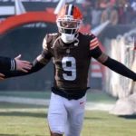 Der Footballspieler Grant Delpit, der ein braun-orangefarbenes Trikot der Browns mit der Nummer 9 trägt, gibt den Fans High-Fives, während er aus einem Tunnel auf das Spielfeld läuft. Alt-Text wurde KI-generiert.