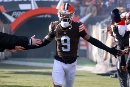 Der Footballspieler Grant Delpit, der ein braun-orangefarbenes Trikot der Browns mit der Nummer 9 trägt, gibt den Fans High-Fives, während er aus einem Tunnel auf das Spielfeld läuft. Alt-Text wurde KI-generiert.