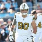 Ein Footballspieler in einem weißen Trikot der New Orleans Saints mit der Rückennummer 90, Bryan Bresee, steht während eines Spiels auf dem Spielfeld; im Hintergrund sind Teamkollegen und Fans zu sehen. Alt-Text wurde KI-generiert.