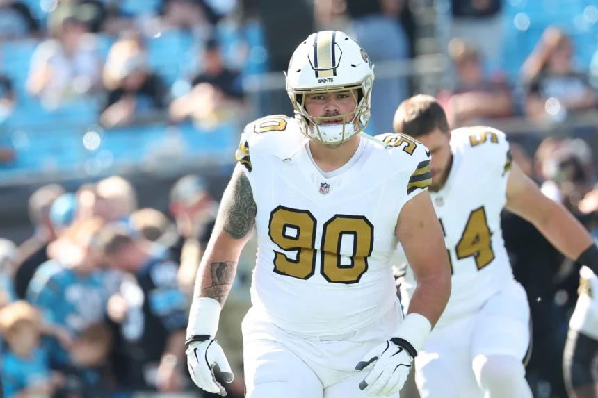 Ein Footballspieler in einem weißen Trikot der New Orleans Saints mit der Rückennummer 90, Bryan Bresee, steht während eines Spiels auf dem Spielfeld; im Hintergrund sind Teamkollegen und Fans zu sehen. Alt-Text wurde KI-generiert.