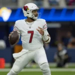 Ein Footballspieler im weißen Trikot der Arizona Cardinals bereitet sich während eines Spiels auf einen Pass vor, hält den Ball mit beiden Händen fest und blickt nach vorne auf das Spielfeld – eine Geste, die an Jacoby Brissetts gelassene Ausstrahlung unter Druck erinnert. Alt-Text wurde KI-generiert.