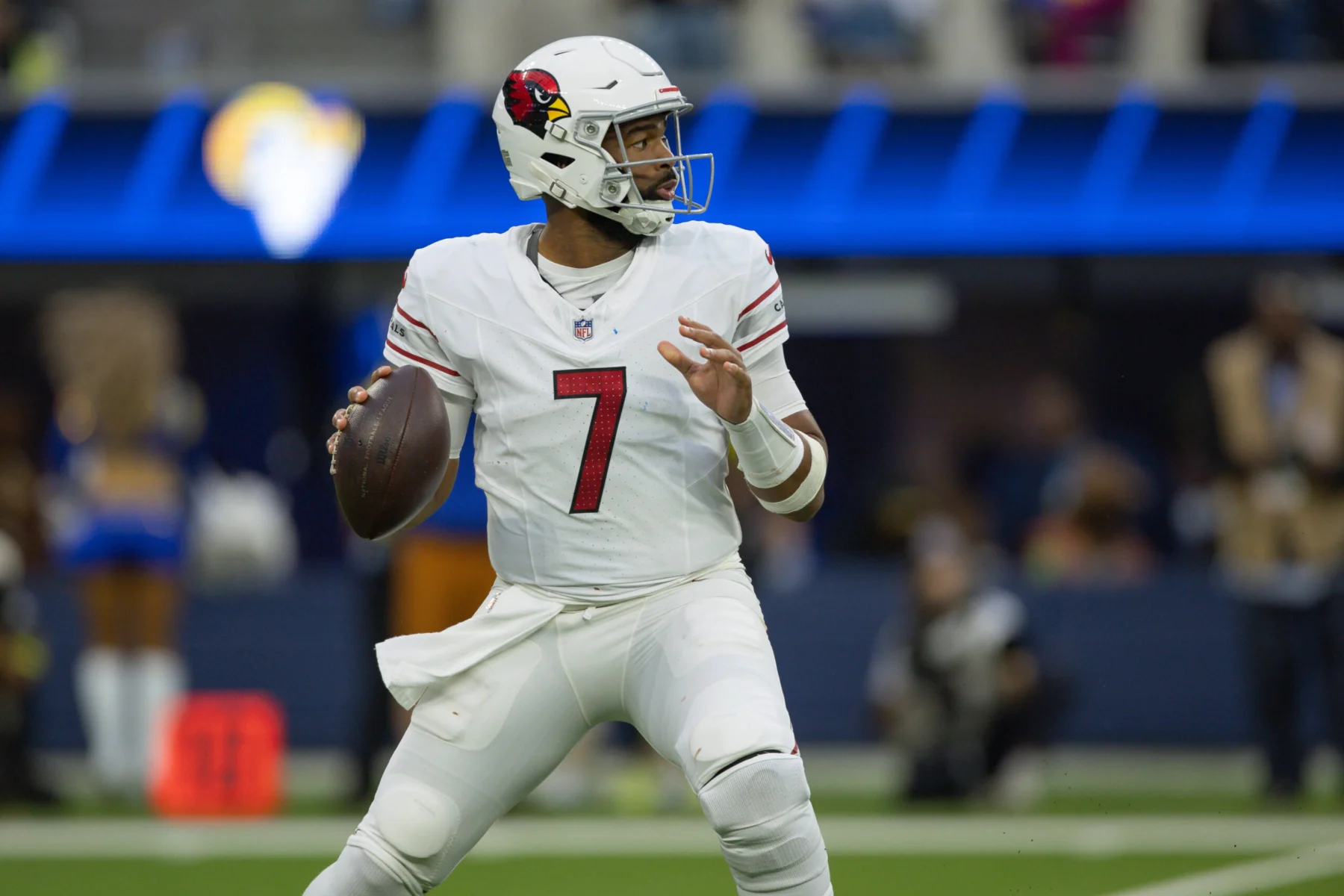 Ein Footballspieler im weißen Trikot der Arizona Cardinals bereitet sich während eines Spiels auf einen Pass vor, hält den Ball mit beiden Händen fest und blickt nach vorne auf das Spielfeld – eine Geste, die an Jacoby Brissetts gelassene Ausstrahlung unter Druck erinnert. Alt-Text wurde KI-generiert.