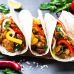 Drei knusprige Chicken-Tacos mit gegrilltem Gemüse und frischen Kräutern, serviert auf einem Holzbrett, garniert mit Limettenschnitzen, Petersilie und Paprika – ein Genuss, als kämen sie frisch aus dem Ofen. Alt-Text wurde KI-generiert.