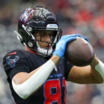 Jayden Higgins, ein Footballspieler im Trikot der Houston Texans, hält einen Football mit beiden Händen fest und bereitet sich während eines Spiels auf einen Spielzug vor. Alt-Text wurde KI-generiert.