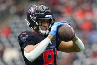 Jayden Higgins, ein Footballspieler im Trikot der Houston Texans, hält einen Football mit beiden Händen fest und bereitet sich während eines Spiels auf einen Spielzug vor. Alt-Text wurde KI-generiert.