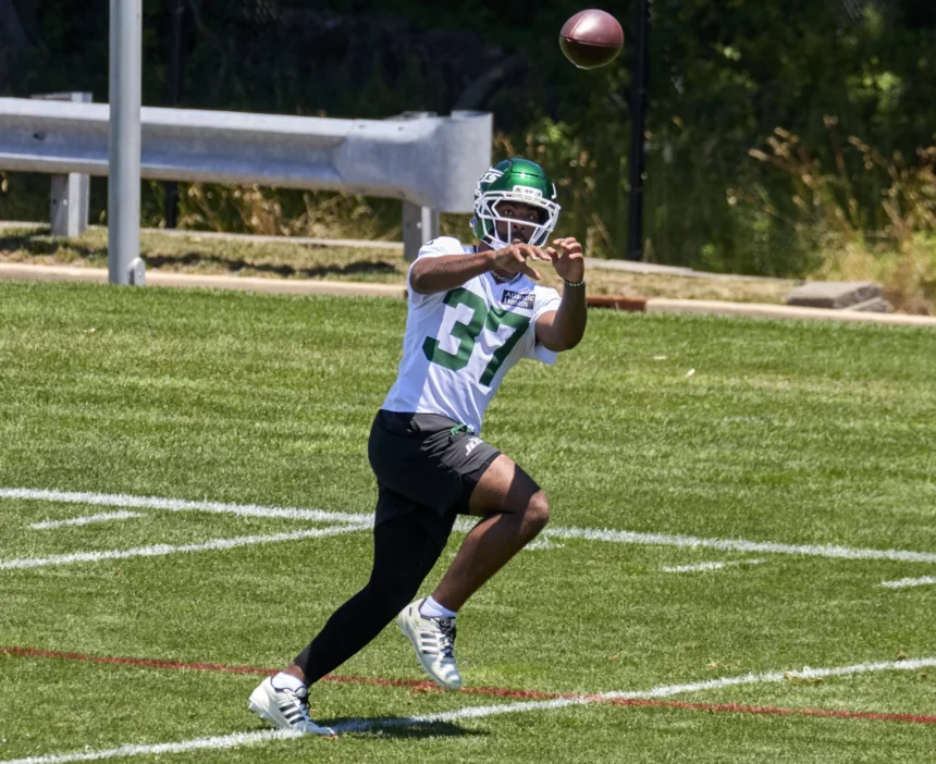 Ein Footballspieler mit weißem Helm und grünem Jets-Trikot mit der Nummer 37, Qwan’tez Stiggers, rennt während des Trainings über das Spielfeld und fängt dabei einen Football. Alt-Text wurde KI-generiert.