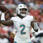Malik Willis - Ein Footballspieler der Miami Dolphins in weißem Trikot und Helm macht sich während eines Spiels gegen die Commanders bereit, den Football zu werfen. Alt-Text wurde KI-generiert.