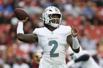 Malik Willis - Ein Footballspieler der Miami Dolphins in weißem Trikot und Helm macht sich während eines Spiels gegen die Commanders bereit, den Football zu werfen. Alt-Text wurde KI-generiert.