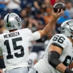 Fernando Mendoza - Ein Footballspieler der Raiders mit der Rückennummer 15 macht sich während eines Spiels bereit, einen Pass zu werfen; im Vordergrund sind seine Teamkollegen von den Raiders zu sehen. Alt-Text wurde KI-generiert.