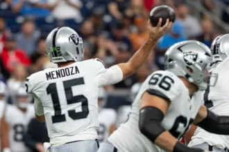 Fernando Mendoza - Ein Footballspieler der Raiders mit der Rückennummer 15 macht sich während eines Spiels bereit, einen Pass zu werfen; im Vordergrund sind seine Teamkollegen von den Raiders zu sehen. Alt-Text wurde KI-generiert.