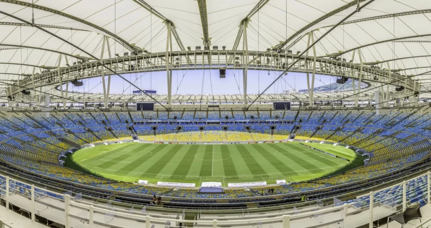 Rio de Janeiro- Weitwinkelaufnahme eines leeren, modernen Stadions mit einem teilweise überdachten Dach, einem grünen Rasenfeld und blauen und gelben Sitzplätzen rund um das Spielfeld; die NFL ist zuversichtlich, dass die Platzverhältnisse für die bevorstehenden Veranstaltungen optimal sind. Alt-Text wurde KI-generiert.