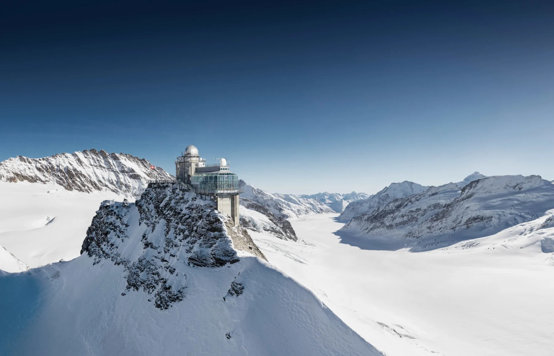 Auf einem schneebedeckten Berggipfel thront eine Forschungsstation, umgeben von verschneiten Hängen und fernen Bergketten unter einem strahlend blauen Himmel – so ruhig und standhaft wie Adam Vinatieri, wenn er sich für einen spielentscheidenden Kick aufstellt. Alt-Text wurde KI-generiert.