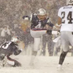 Adam Vinatieri - Ein Footballspieler zeigt die Präzision eines Adam Vinatieri, als er während eines verschneiten Spiels im Schatten der Alpen ein Field Goal schießt, während seine Teamkollegen den Ball halten und die gegnerischen Spieler versuchen, den Schuss zu blocken. Alt-Text wurde KI-generiert.