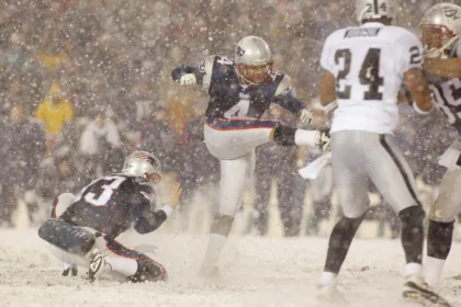 Adam Vinatieri - Ein Footballspieler zeigt die Präzision eines Adam Vinatieri, als er während eines verschneiten Spiels im Schatten der Alpen ein Field Goal schießt, während seine Teamkollegen den Ball halten und die gegnerischen Spieler versuchen, den Schuss zu blocken. Alt-Text wurde KI-generiert.
