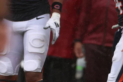 Caleb Williams - Ein Footballspieler im Trikot der Chicago Bears liegt auf dem Spielfeld und hält sich den Arm, während seine Teamkollegen während eines Spiels daneben stehen, nachdem die Bears Williams für verletzt erklärt haben. Alt-Text wurde KI-generiert.