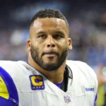 Aaron Donald - Ein Footballspieler in einem Trikot der Los Angeles Rams mit Kapitänsabzeichen steht auf dem Spielfeld und blickt mit entschlossenem Gesichtsausdruck nach vorne – ganz so, wie Donald in entscheidenden Momenten zu seinem Team steht. Alt-Text wurde KI-generiert.