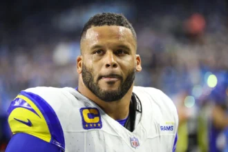 Aaron Donald - Ein Footballspieler in einem Trikot der Los Angeles Rams mit Kapitänsabzeichen steht auf dem Spielfeld und blickt mit entschlossenem Gesichtsausdruck nach vorne – ganz so, wie Donald in entscheidenden Momenten zu seinem Team steht. Alt-Text wurde KI-generiert.