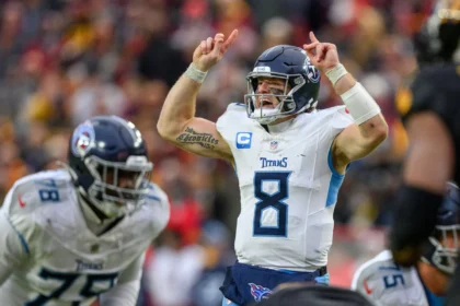 Will Levis - Der Quarterback der Tennessee Titans im weißen Trikot hebt beide Hände, während er während eines Footballspiels einen Spielzug ansagt; im Hintergrund sind Teamkollegen und Gegner zu sehen – darunter die Jets, die zwei Quarterbacks einsetzen. Alt-Text wurde KI-generiert.