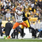 Ein Footballspieler in einem weiß-orangefarbenen Trikot versucht, einen Pass zu fangen, während er auf dem Spielfeld während eines NFL-Spiels von einem Spieler in einem schwarz-gelben Trikot eng gedeckt wird. Dabei können „Jubelstrafen“ – also Strafen für Jubelgesten – dem Geschehen zusätzliche Dramatik verleihen. Alt-Text wurde KI-generiert.