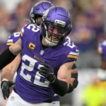 Ein Footballspieler in einem violetten Trikot und Helm der Minnesota Vikings läuft während eines Spiels über das Spielfeld, im Hintergrund sind seine Teamkollegen zu sehen, während der Bericht „Vikings holen Harrison Smith“ die starke Defensivaufstellung des Teams unterstreicht. Alt-Text wurde KI-generiert.